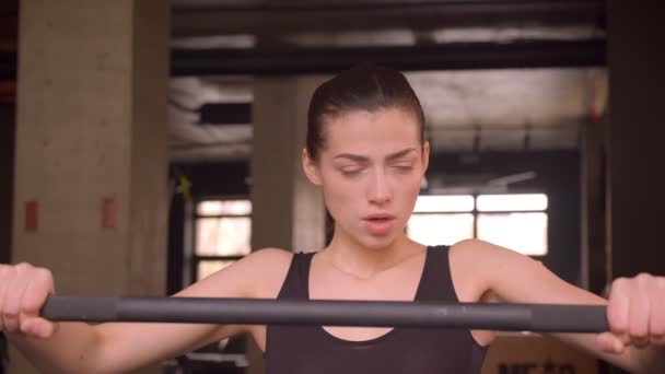 Tiro de perto de jovem atleta atraente feminino andando e se preparando para levantar pesos com determinação no ginásio dentro de casa — Vídeo de Stock