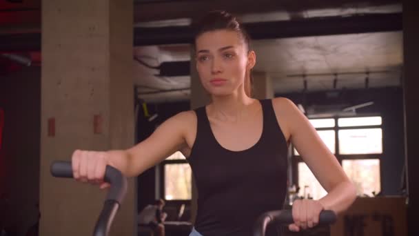 Closeup shoot of young attractive athlete female with ponytail working out on the orbitrek in the gym indoors — Stock Video