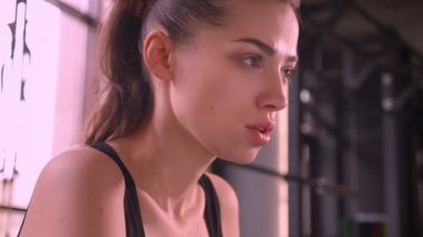 Spor salonunda oturan ve ileri kapalı motive yüz ifadesi ile ağır nefes arayan genç çekici atlet kadın Closeup ateş