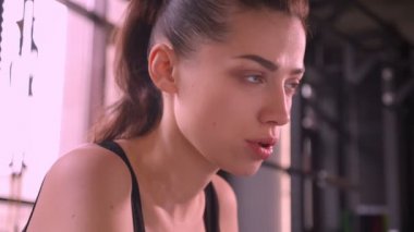 Spor salonunda oturan ve ileri ye dönük genç fit atlet kadın Closeup ateş kapalı motive yüz ifadesi ile ağır nefes