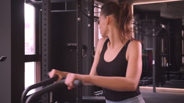 Nahaufnahme Shooting der jungen attraktiven Athletin gesunde Frau mit Pferdeschwanz beim Training auf dem Orbitrek motiviert in der Turnhalle — Stockvideo