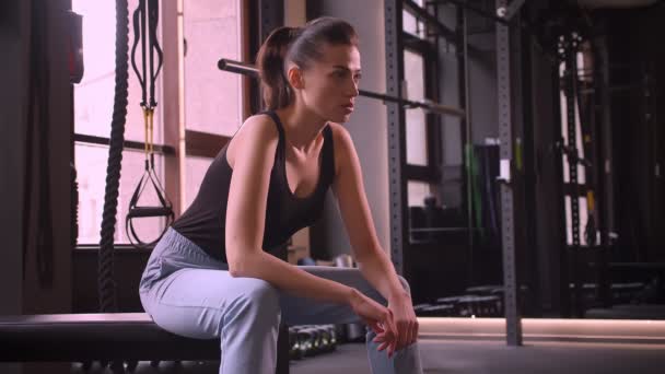 Zbliżenie strzelać młodych atrakcyjny sportowiec kobiet siedzi w siłowni patrząc na aparat z motywacją wyraz twarzy w pomieszczeniu — Wideo stockowe