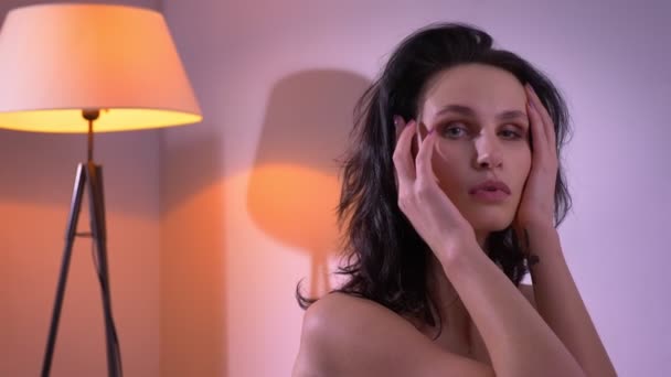 Portrét sexy brunetového modelu v černém prádle, který si upevní vlasy v svůdném sledování kamery v domácí atmosféře. — Stock video