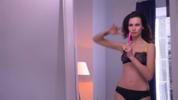 Close-up espelho reflexo de modelo morena sexy em lingerie preta canta em uma escova e dança ativamente em casa . — Vídeo de Stock