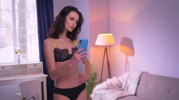 Portrét hezkou a sexy brunetového modelu v černém prádle, kde se v zrcadle dělá fotografie doma. — Stock video
