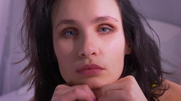 Close-up shot of attractive brunette model leaning on hands watches modestly and calmly into camera at home. — Stock Video