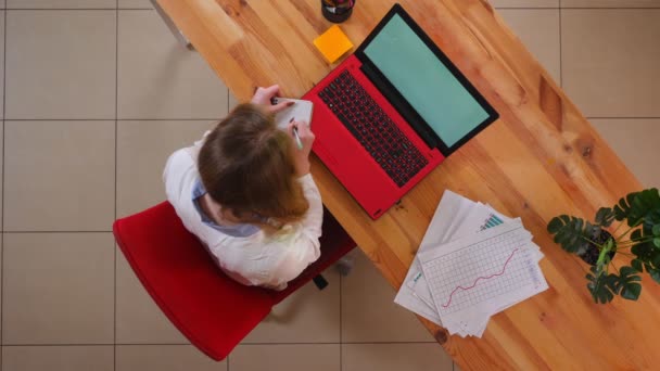 Close-up top shoot de jovem mulher de negócios caucasiana digitando no laptop e tomar notas dentro de casa no escritório — Vídeo de Stock