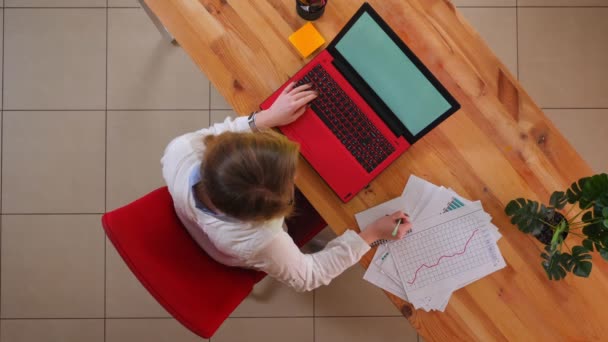 Gambar close-up atas dari wanita bisnis muda Kaukasia yang bekerja pada laptop dan mencatat di dalam ruangan di kantor — Stok Video