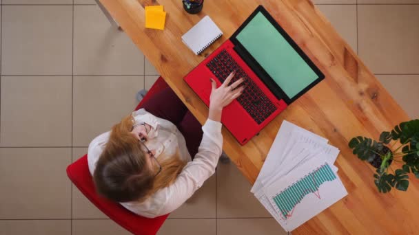 Close-up top shoot van jonge Kaukasische zakenvrouw met een telefoontje zittend in de voorkant van de laptop binnenshuis in het kantoor — Stockvideo