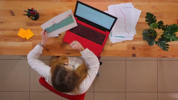 Tiro superior close-up de jovem funcionário caucasiano usando o laptop e analisando gráficos dentro do escritório — Vídeo de Stock