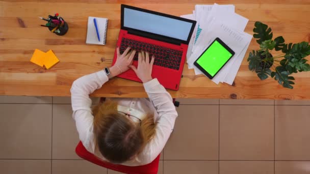 Primo piano ripresa superiore di giovane dipendente caucasico che lavora sul computer portatile con il tablet con schermo verde sdraiato sulla scrivania all'interno dell'ufficio — Video Stock