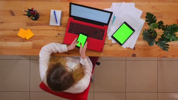 Close-up top shoot van jonge blanke werknemer met behulp van de telefoon met de Tablet met groen scherm liggend op het Bureau binnenshuis in het kantoor — Stockvideo