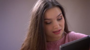 Genç güzel esmer beyaz beyaz kadın tablet tesniye closeup ateş mutlu gülümseyerek ve kapalı rahat bir dairede kameraya bakarak