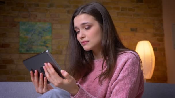 Closeup shoot of young pretty brunette caucasian female using the tablet beind sad and upset in a cozy apartment indoors — Stock Video