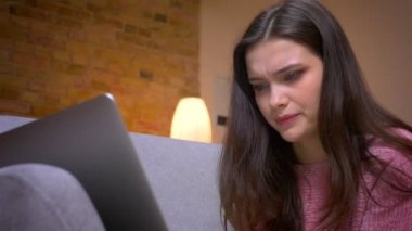 Dizüstü bilgisayarda komik bir video izlerken ve kapalı rahat bir dairede kanepede eğlenen genç güzel esmer kafkas kadın Closeup ateş