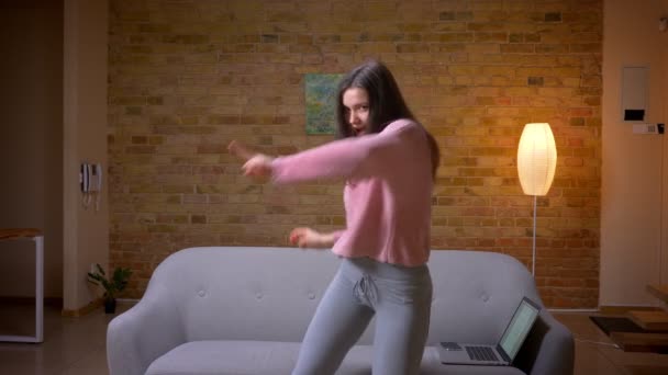 Съемки крупным планом молодой красивой брюнетки кавказской женщины, танцующей смеясь и веселясь в уютной квартире в помещении — стоковое видео