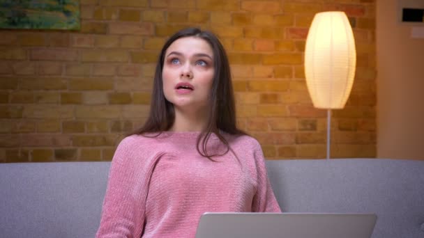 Closeup shoot of young pretty brunette caucasian female teenager using the laptop and smiling sitting on the couch in a cozy apartment indoors — Stock Video