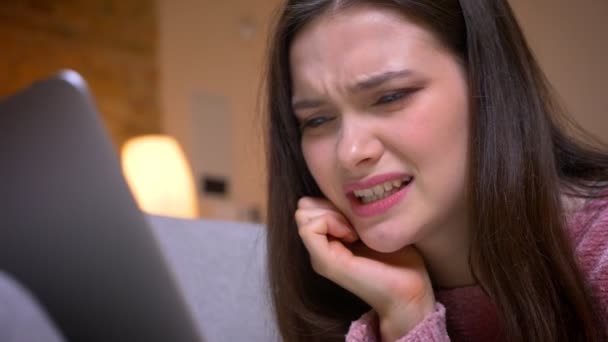 Close-up tiro de jovem bonita morena branca adolescente do sexo feminino ter uma chamada de vídeo no laptop e reagindo com nojo no sofá em um aconchegante apartamento dentro de casa — Vídeo de Stock