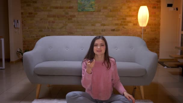Крупним планом знімок молодої красивої брюнетки біла жінка дивиться телевізор з хвилюванням сидячи на дивані в затишній квартирі в приміщенні — стокове відео