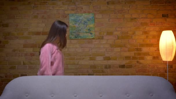 若いかわいいブルネットの女性がソファの後ろを歩いて、魔法のトリックを実行して消えるクローズアップ撮影 — ストック動画