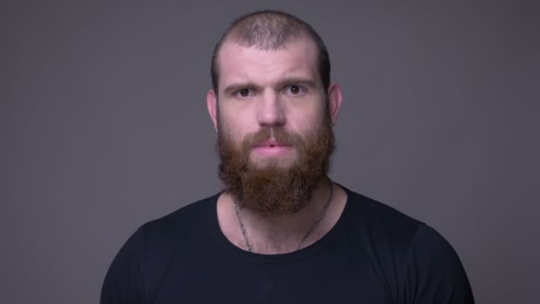 Closeup shoot of adult handsome muscular caucasian man with beard being confused looking at camera with background isolated on gray — Stock Video