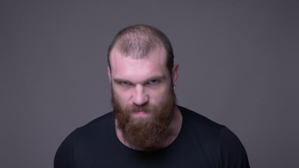 Närbild shoot of Adult stilig muskulös kaukasiska man med skägg är arg tittar på kamera med bakgrund isolerad på grå — Stockvideo