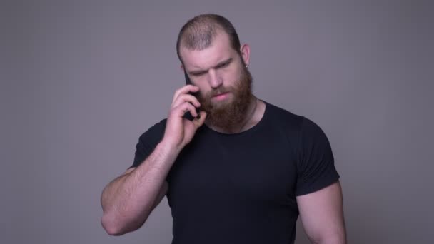 Zbliżenie strzelać dorosłego przystojnego mięśni kaukaski mężczyzna z brodą o telefon przed kamerą z tła izolowane na szarym — Wideo stockowe