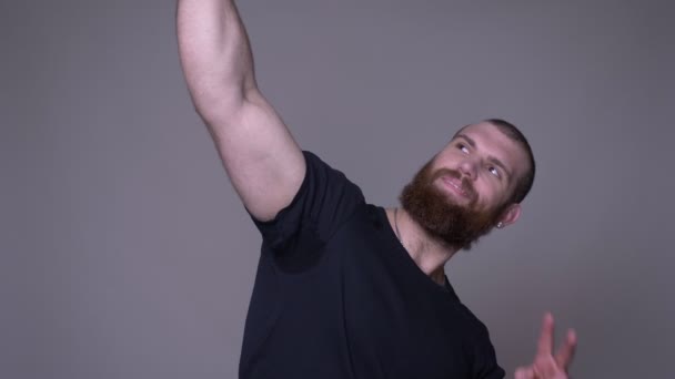 Closeup shoot of adult handsome muscular caucasian man with beard having a video call on the phone in front of the camera with background isolated on gray — Stock Video