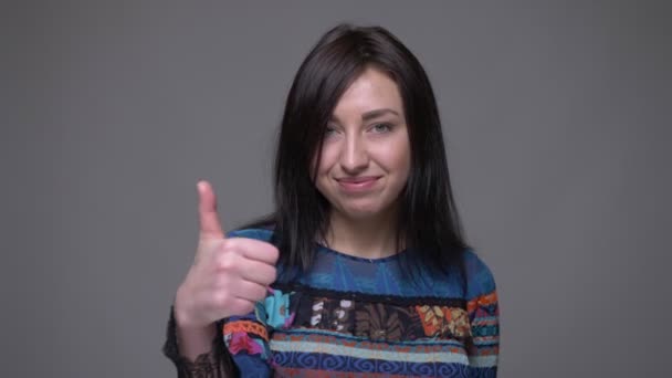 Close-up portret van volwassen Kaukasische brunette vrouw toont duim omhoog kijken naar camera met achtergrond geïsoleerd op grijs — Stockvideo