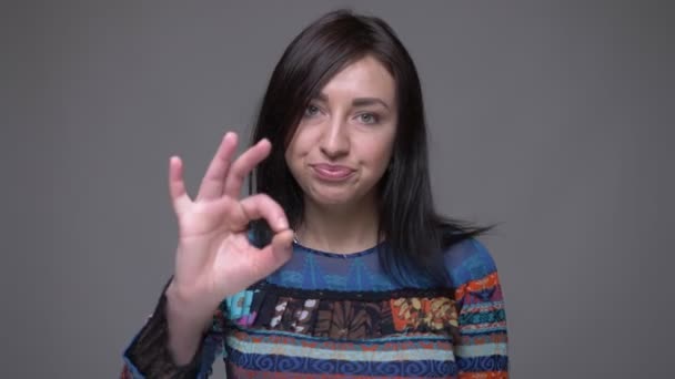 Close-up retrato de adulto caucasiano morena feminino mostrando OK handsign olhando para a câmera com fundo isolado no cinza — Vídeo de Stock