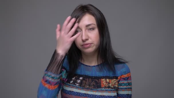 Портрет крупным планом взрослой брюнетки кавказской женщины, закрывающей голову смущенным взглядом на камеру с изолированным на сером фоне — стоковое видео