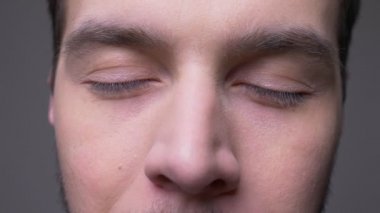 Gözleri kameranın kapalı olmasına ve arka planın gri üzerinde izole edilmiş olarak açılmasına bakan genç erkek yüzün yakın çekim çekimi