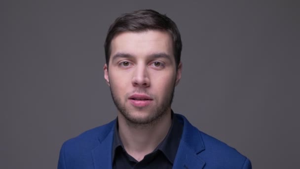 Nahaufnahme eines jungen gutaussehenden kaukasischen Mannes, der lächelnd und nickend in die Kamera schaut, mit isoliertem Hintergrund auf grau — Stockvideo