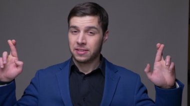 Parmaklarını çapraz olan genç yakışıklı beyaz adam Closeup çekim gri izole arka plan ile kamera bakarak umutlu ve endişeli olmak