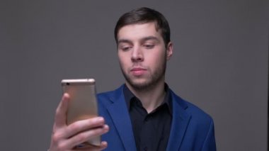 Genç yakışıklı beyaz adam gri izole arka plan ile kamera önünde telefonda bir görüntülü arama olan Closeup ateş