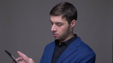 Gri üzerinde izole arka plan ile kamera önünde tablet üzerinde ağ tarama genç yakışıklı beyaz adam Closeup ateş