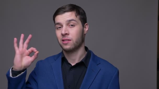 Close-up shoot van jonge knappe blanke man toont oke teken kijken naar camera met achtergrond geïsoleerd op grijs — Stockvideo