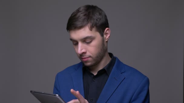 Primer plano de brote de joven guapo hombre caucásico utilizando la tableta y mostrando la pantalla verde a la cámara con fondo aislado en gris — Vídeos de Stock