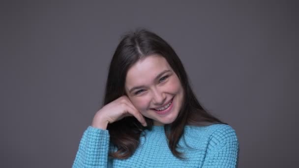 Closeup shoot of young pretty brunette female smiling cheerfully looking at camera with background isolated on gray — Stock Video