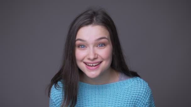 Närbild shoot av ung Söt brunett kvinna överraskas leende glatt tittar på kamera med bakgrund isolerade på grått — Stockvideo