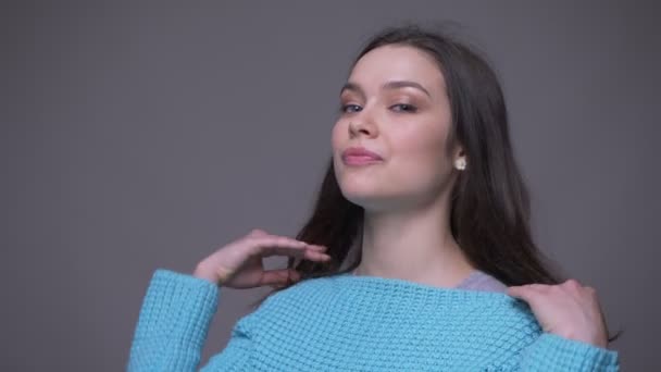 Närbild shoot av ung Söt brunett kvinnlig leende förföriskt och gungade hennes hår tittar på kamera med bakgrund isolerade på grått — Stockvideo