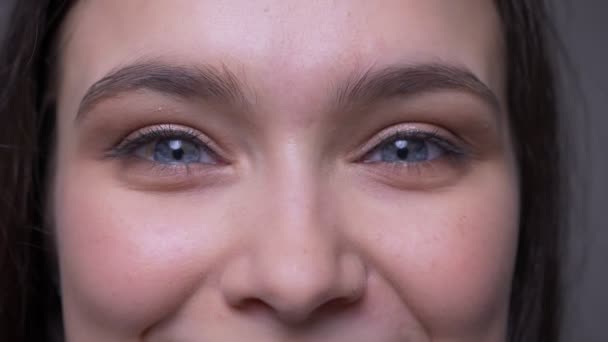 Съемки крупным планом молодого привлекательного женского лица с синими сверкающими глазами, смотрящими в камеру с улыбкой на лице — стоковое видео
