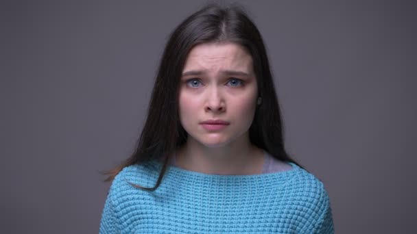 Съемки крупным планом молодой брюнетки грустной женщины, смотрящей в камеру с изолированным на сером фоне — стоковое видео