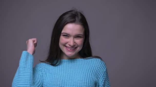 Close-up shoot van jonge mooie brunette vrouw gebaren een duim omhoog en glimlachend kijken naar camera met achtergrond geïsoleerd op grijs — Stockvideo