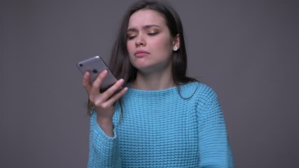 Close-up shoot van jonge mooie brunette vrouwelijke texting op de telefoon met achtergrond geïsoleerd op grijs — Stockvideo