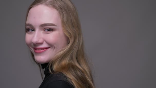 Nahaufnahme Porträt einer jungen attraktiven brünetten Frau, die sich dreht und glücklich lächelnd in die Kamera blickt, mit isoliertem Hintergrund auf grau — Stockvideo