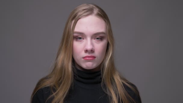 Крупный план портрет молодой привлекательной брюнетки, грустной и подавленной, смотрящей в камеру с изолированным на сером фоне — стоковое видео