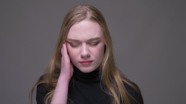 Крупный план портрета молодой привлекательной брюнетки женщины, страдающей головной болью и истощенной на фоне, изолированном на сером — стоковое видео