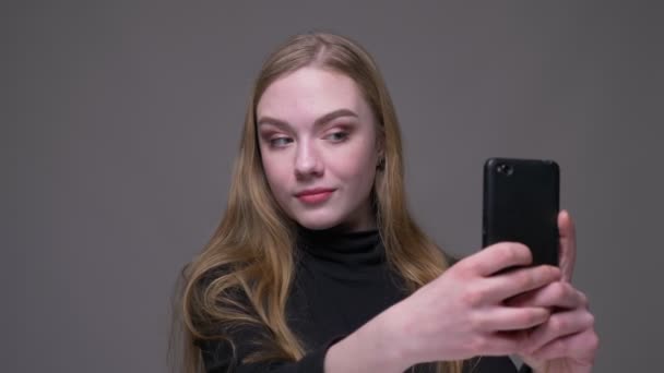 Gros plan portrait de jeune belle brune femelle prenant selfies sur le téléphone avec fond isolé sur gris — Video