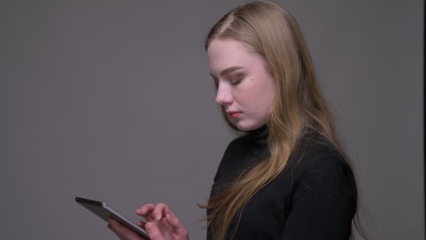 Портрет крупным планом молодой привлекательной брюнетки с женскими текстами на планшете на фоне, изолированном на сером — стоковое видео